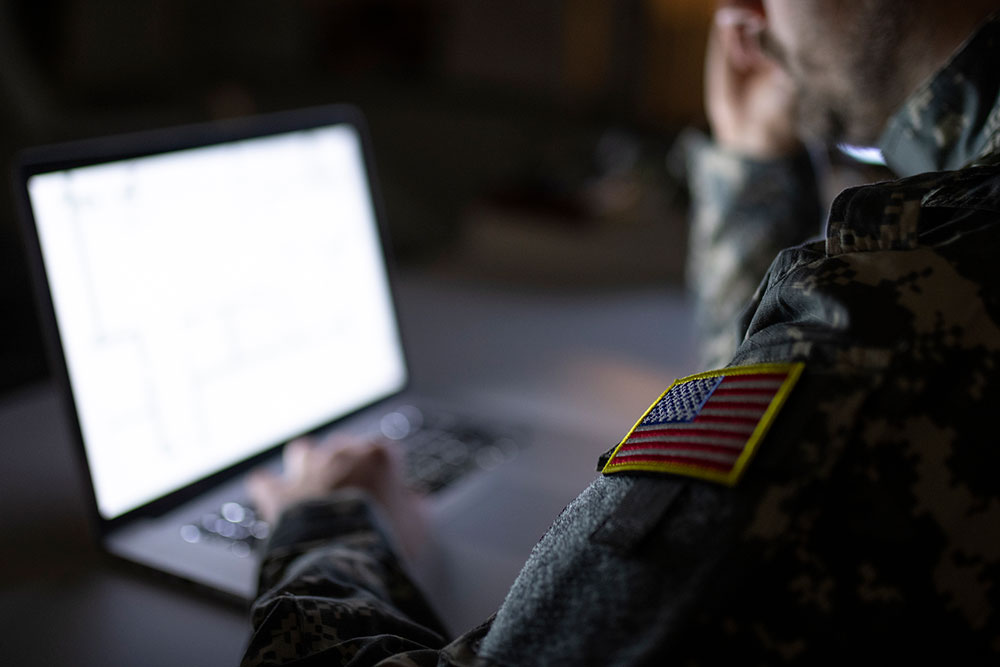 U.S. soldier in uniform typing on a computer that has code up on the screen
